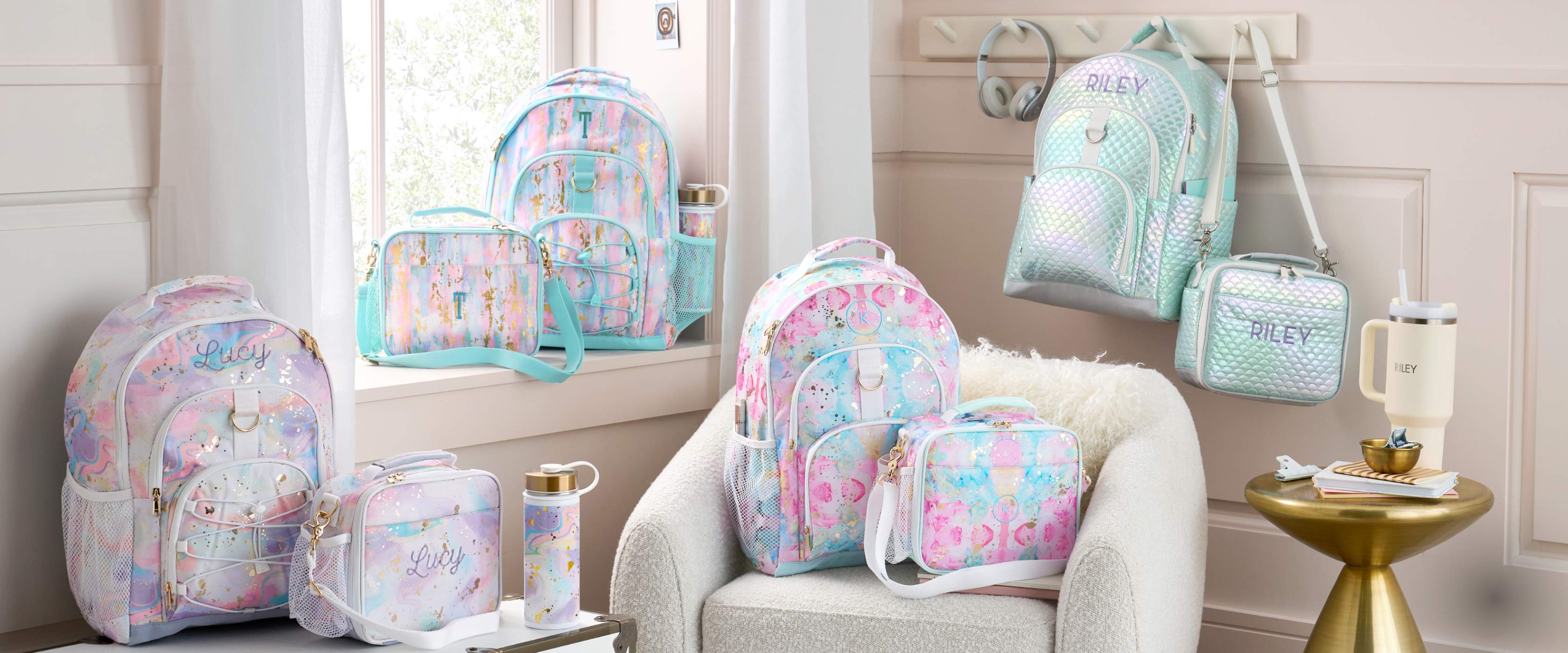 3 Luggage bags with similar color schemes including dark gray, light pink, and white, all of which have monogrammed personalizations, lie on top of an off white wood paneled background.