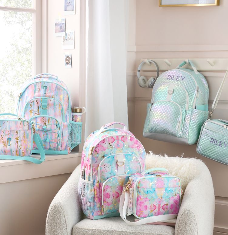 3 duffel bags with flower and striped patterns in blue and white colors, are stacked in a row. 3 Luggage bags with similar color schemes including dark gray, light pink, and white, all of which have monogrammed personalizations, lie in a row beneath the duffel bags. All of these luggage options lie on top of an off white wood paneled background.