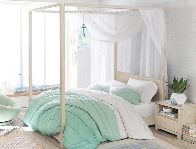 Weathered white wood Costa canopy bed topped with draping white gauze and styled with a light blue duvet.