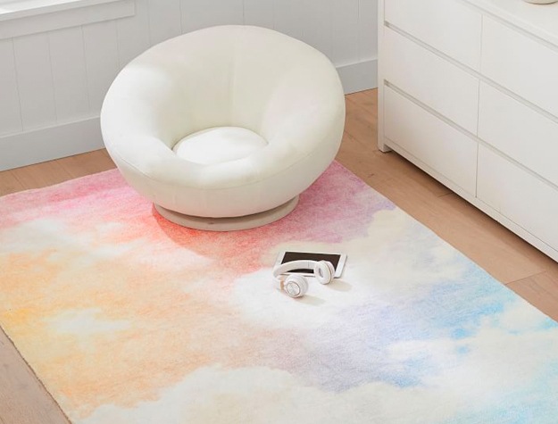 Rainbow Sky Washable Rug against a wood floor, with a white chair, tablet, and headphones on it.