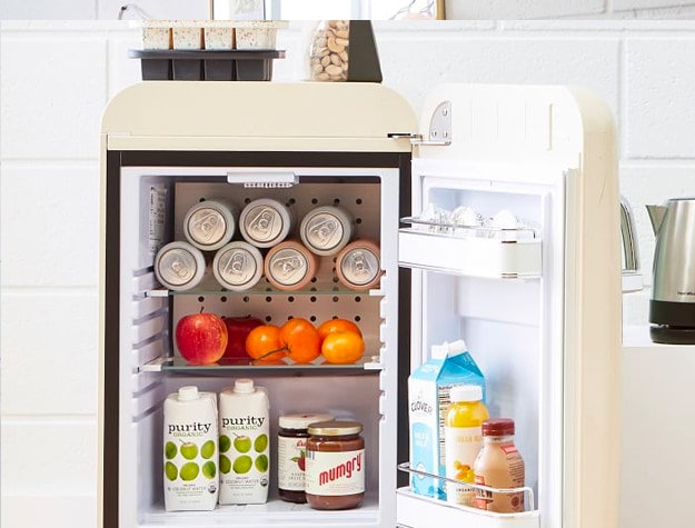 Smeg Mini fridge full of food and drinks, with cans in the top shelf.