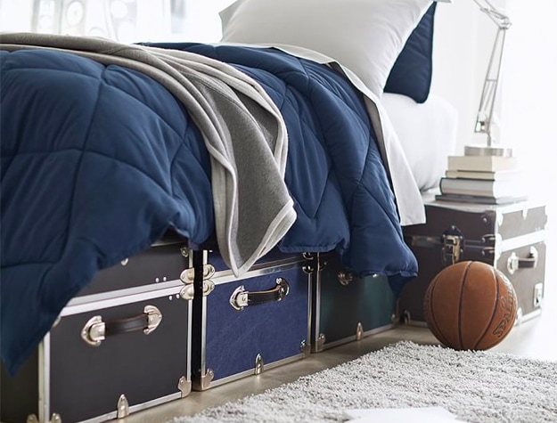 Three XXL Dorm Trunks beneath a bed with a navy comforter.