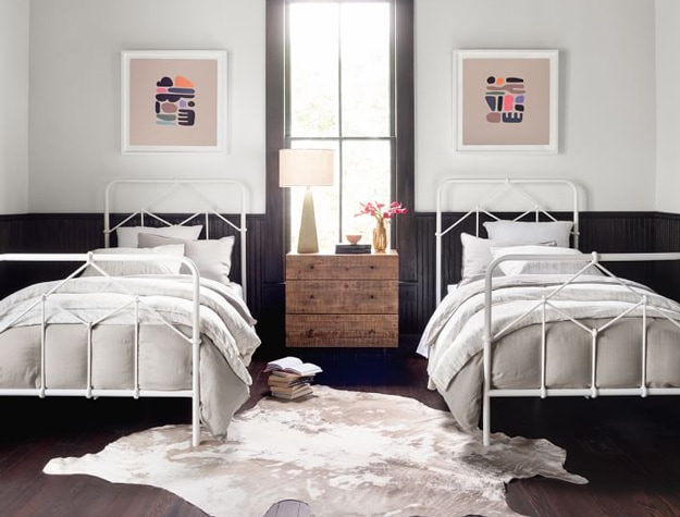 Two twin-sized Casey iron beds styled in a room with a cowhide rug and minimalist wall art.