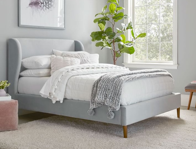 Wren wingback upholstered bed in silver luster velvet styled with a white comforter and gray chenille throw at the foot of the bed. 
