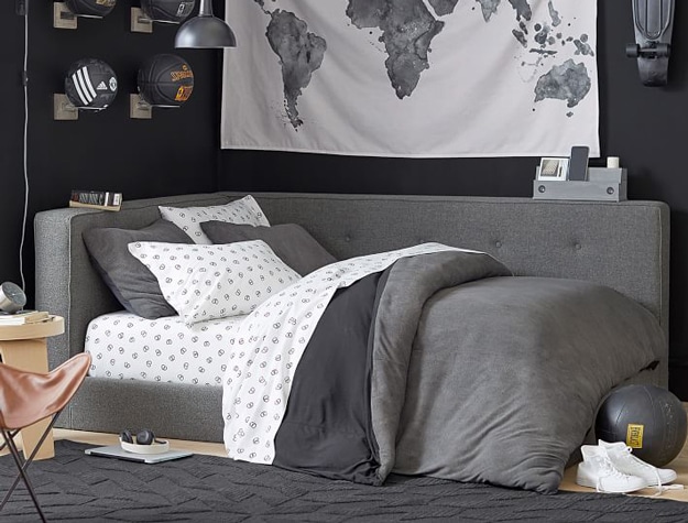 Cushy gray upholstered corner bed styled below a world map tapestry.