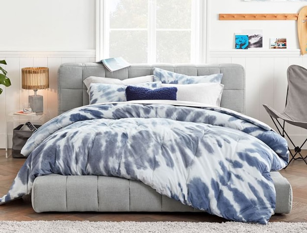 King-sized Baldwin upholstered bed in light gray styled with a blue tie-dye comforter.