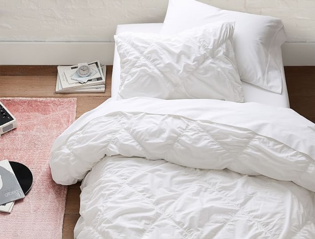 Ruched Diamond Organic Duvet Cover in white styled with a matching pillow sham and white sheets.