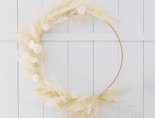 A wreath made with natural pampas and cotton balls hangs on a wall.