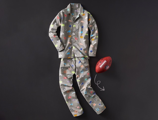 a set of pajamas designed with the logos of every NFL team laying next to a football