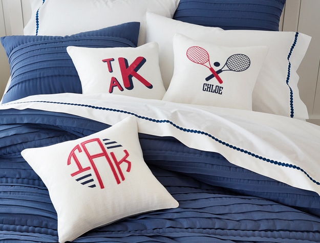 three monogrammed tennis pillows on a bed with navy bedding