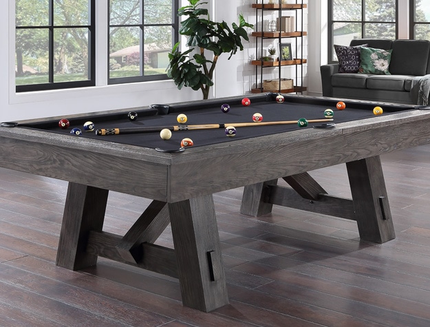 a pool table placed around a loveseat, plant and shelf in an open room