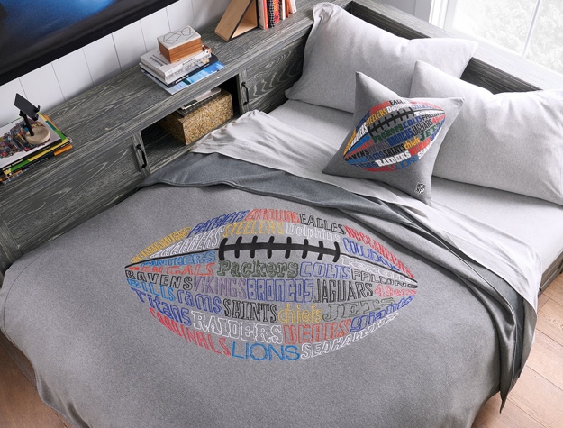a blanket designed with a football lying on a bed with a football throw pillow