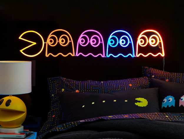 A PAC-MAN LED Wall light above a bed with PAC-MAN sheets.