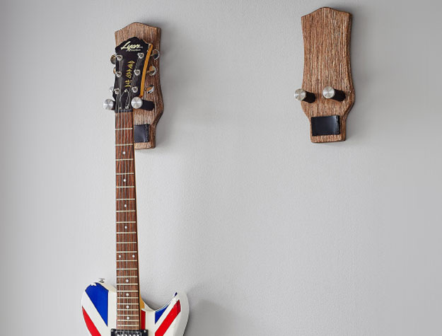 A guitar wall mount with one guitar hanging from it.