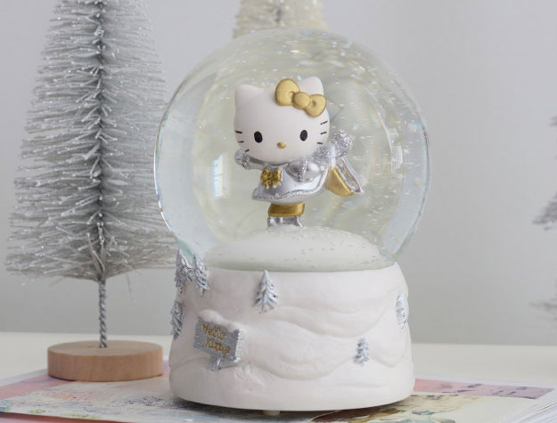 A Hello Kitty&reg; snowglobe next to small Christmas tree decorations.