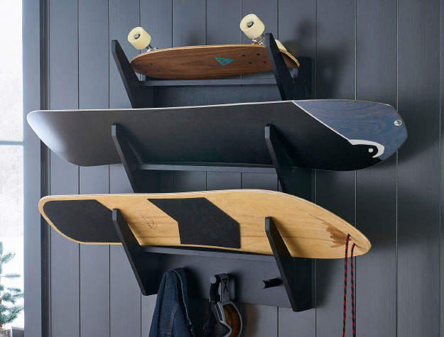 A wall-mounted board rack with two snowboards and a skateboard.