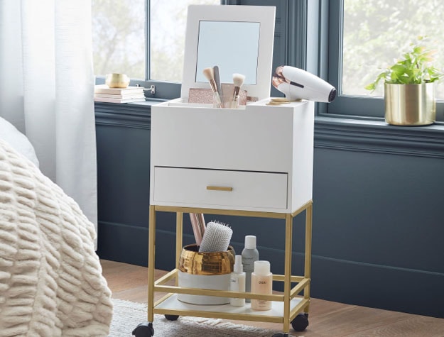 White beauty cart with makeup brushes and a hair dryer on top.