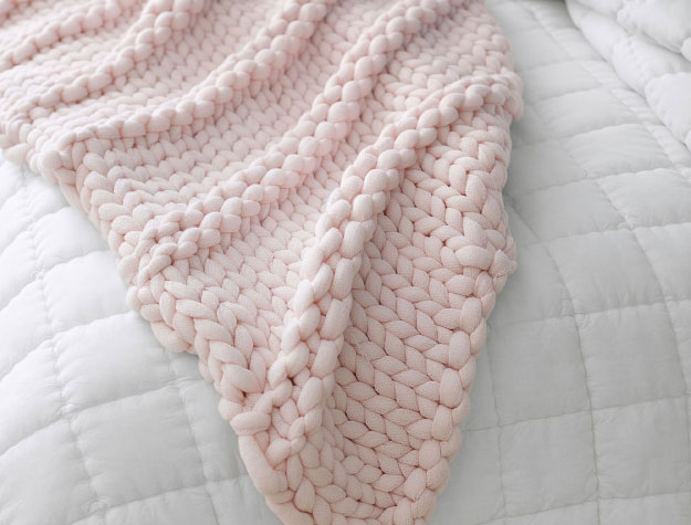 A pink chunky throw blanket on top of a bed.