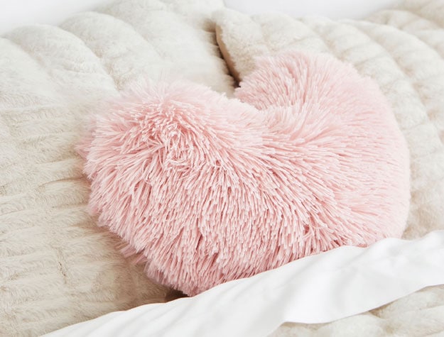 A pink heart pillow on a neatly-made bed.