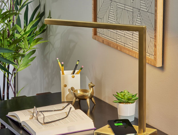 A table lamp on top of a desk with a book and phone.