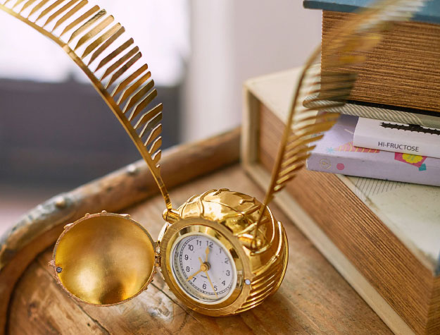 A Golden Snitch clock on a wooden desk.