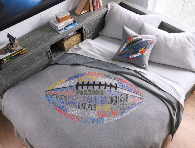 A neatly-made bed with an NFL-themed blanket on top.