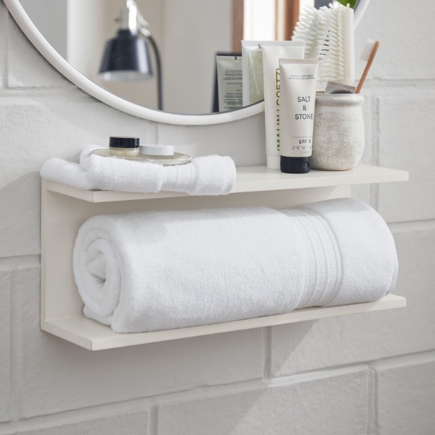 White shelf suctioned to mirror holding makeup products and hair brush.