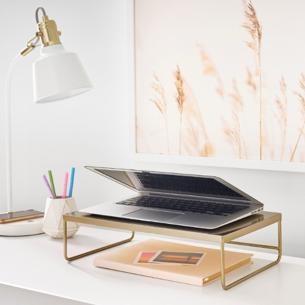 A laptop sits on top of a gold metal desk riser