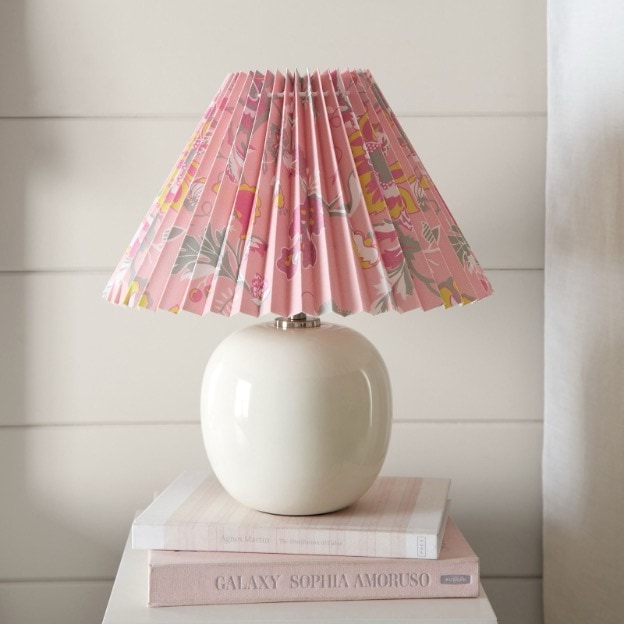 A white table lamp with bright pink floral lampshade sits atop a stack of books