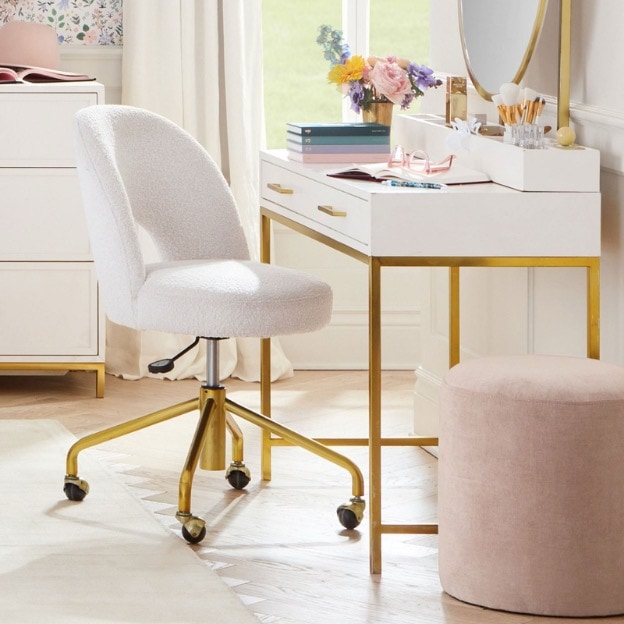 A white boucle desk chair sits in front of a white-and-gold desk vanity.