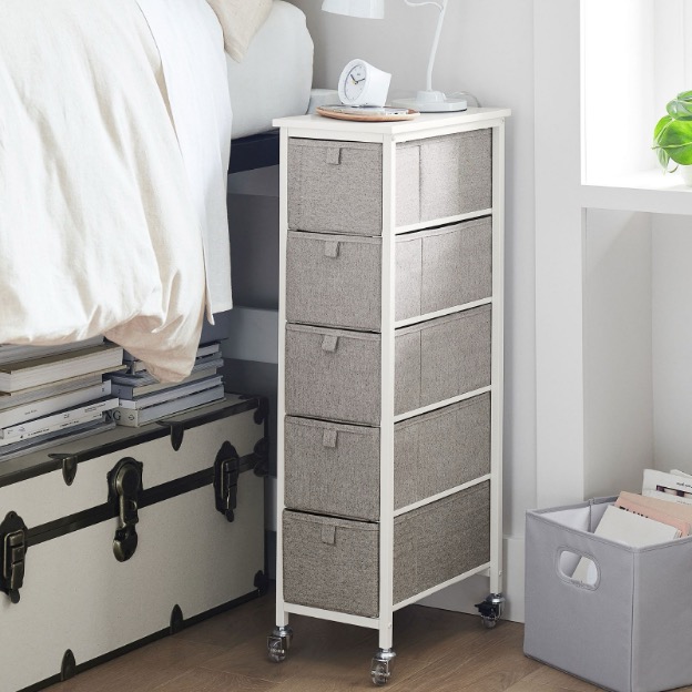 A narrow storage cart on wheels rests next to a dorm bed