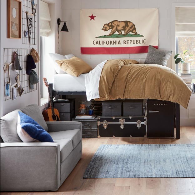 A peek inside of a guy’s dorm bedroom including the underbed storage set-up, bedding, and wall decor