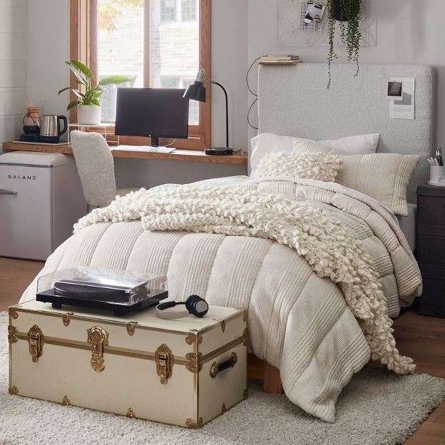 A light beige trunk sits at the foot of a dorm bed 