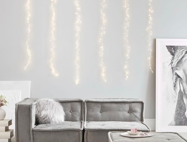 white string lights on wall behind gray sofa