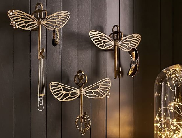 Three jewelry hooks shaped like the winged keys from the Wizarding World of Harry Potter hang in a room.