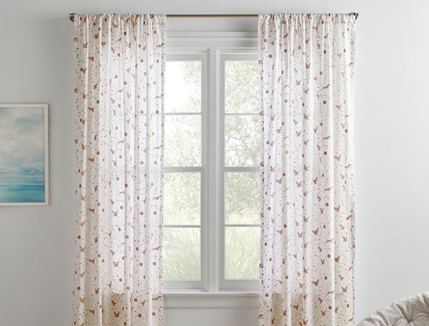 Airy cotton voile curtains patterned with owls, stars, and moons hang in a room.