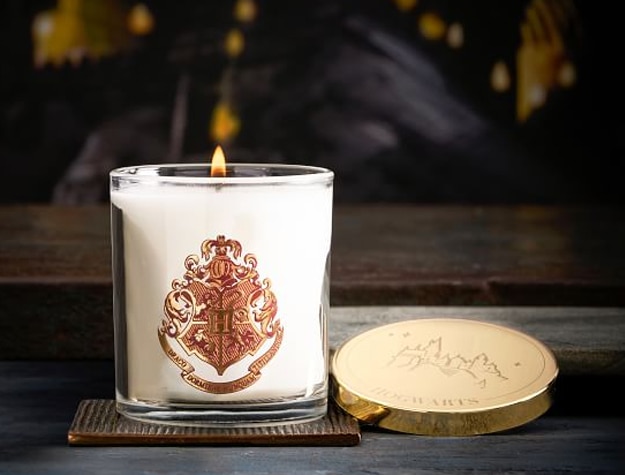 A candle with the Hogwarts crest sits atop a wooden table.