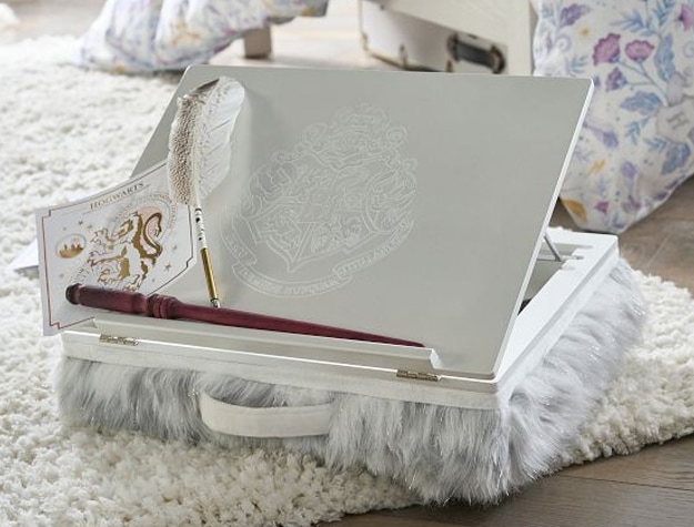 An adjustable lapdesk featuring the Hogwarts crest holds a quill, wand and Hogwarts sticky note. 