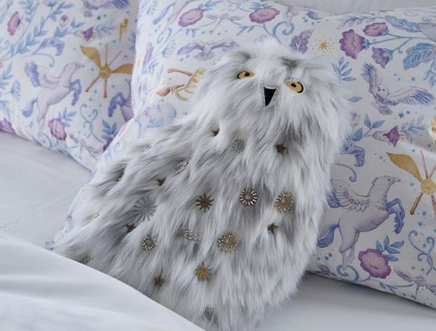 A fuzzy pillow shaped like Harry Potter’s Hedwig rests on top of a bed set.