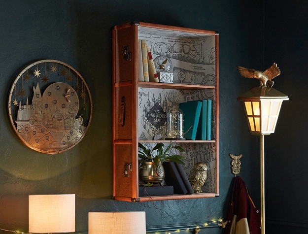 A bookcase shaped like a suitcase hangs on the wall and features lining printed with the Marauder’s Map. 