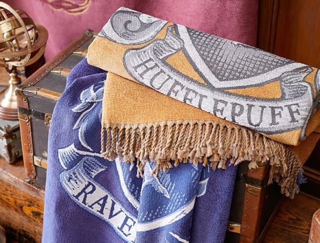 Throws bearing the Hufflepuff and Ravenclaw crests are draped over a chest.