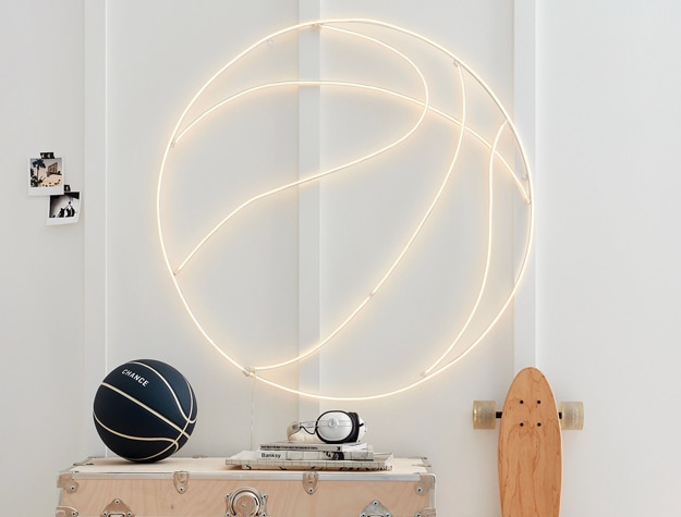 a neon basketball light displayed next to a skateboard, wooden chest and black basketball