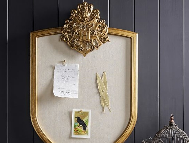 A pinboard shaped like the Hogwarts crest hangs in a room.