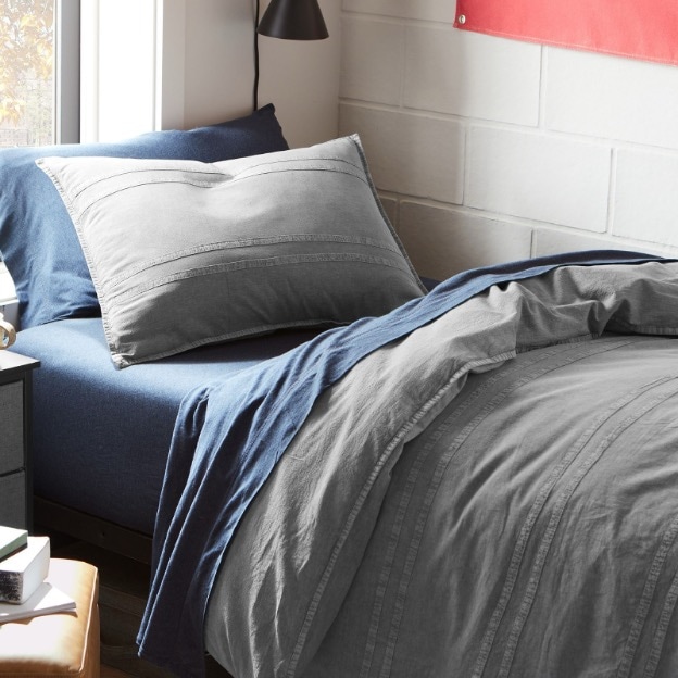 This dorm bed features a grey twin XL duvet cover and navy blue sheets.
