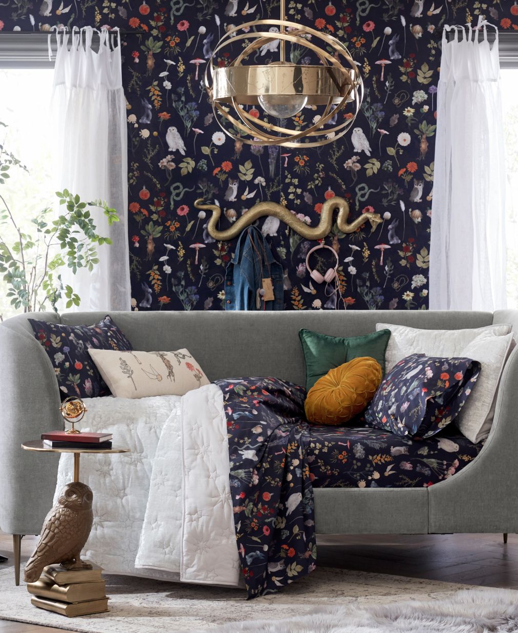 Harry Potter sample designed room. Shows a couch on top of a faux fur rug. The couch is draped with a Harry Potter theme plants and potions blanket in navy with gold, red, and green accents and iconography. The wallpaper behind the couch matches the Harry Potter themed blanket.