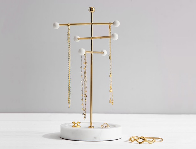 Marble and gold jewelry stand with bracelets and earrings on table