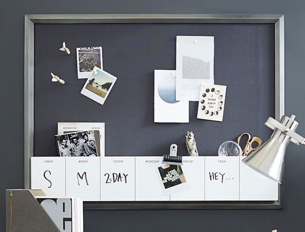 Metal pinboard with dry erase calendar, artwork and images pinned above desk