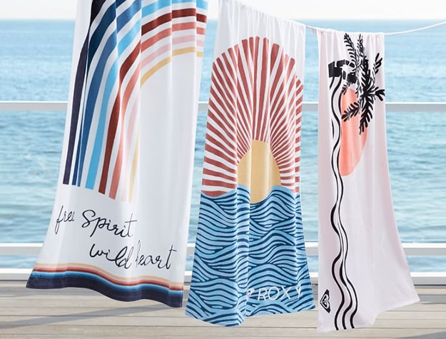 set of patterned sunset beach towels hanging to dry with ocean in background