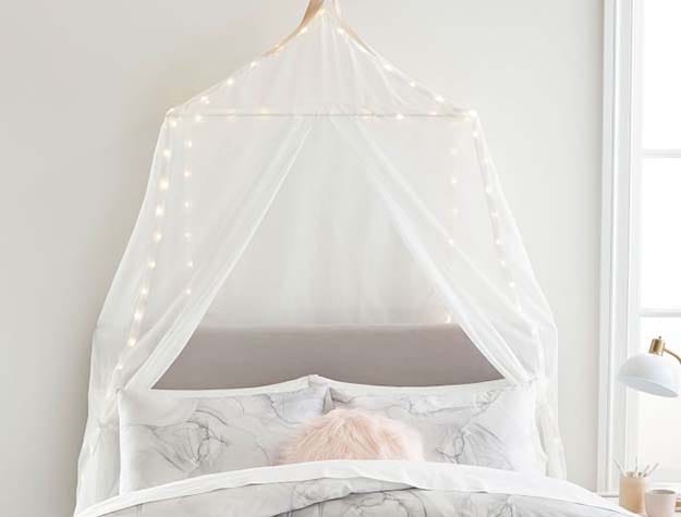 A bed with a rectangular light up fairy light canopy hanging over it