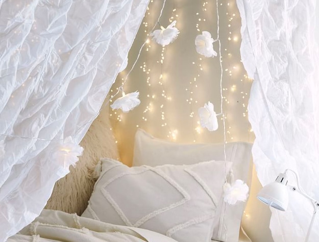 White Flower String Lights hanging above a bed with neutral-colored bedding. 